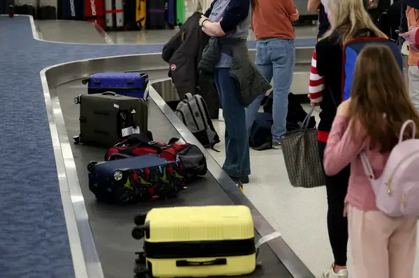 People standing at a baggage claim at an airport with luggage on the conveyor belt
