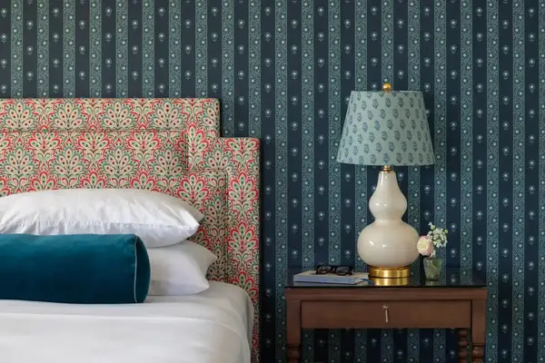 A hotel room with a bed, patterned headboard, side table with a lamp and small decorations