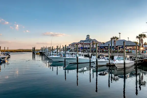 Boats docked at a marina near a waterfront building, dusk sky