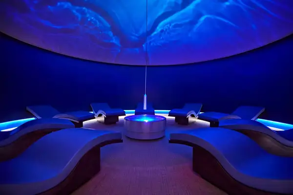 A relaxation room with curved recliners under ambient blue lighting
