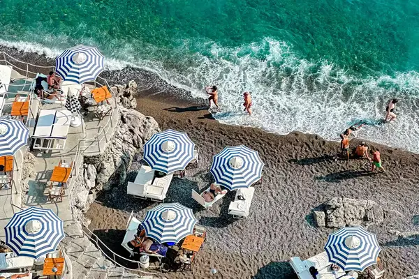 Blue and white striped beach umbrellas and people on a beach in Italy