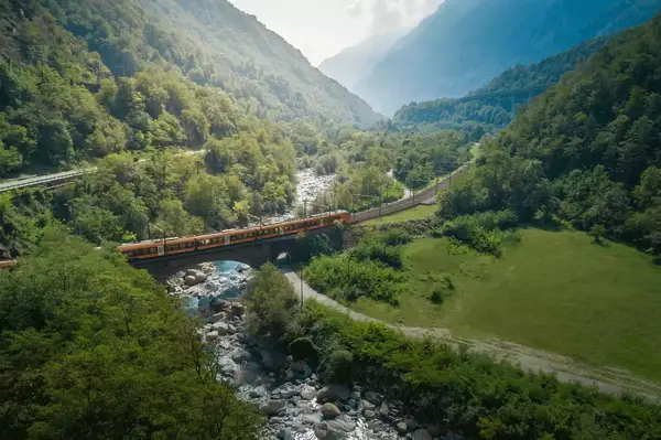 Train crossing a bridge in a scenic Swiss valley among mountains and a river