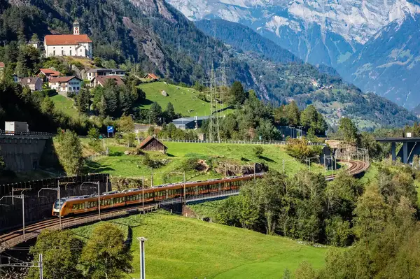 A train traveling through a mountainous landscape with a village and a church on a hillside