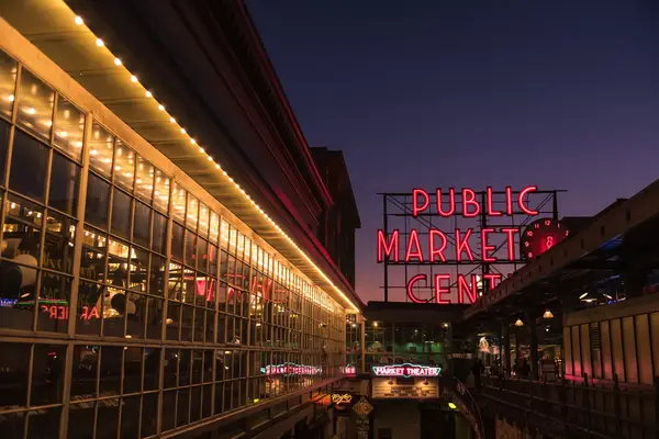 The famous illuminated Pike Place Market sign illuminated at sunset over Post Alley.