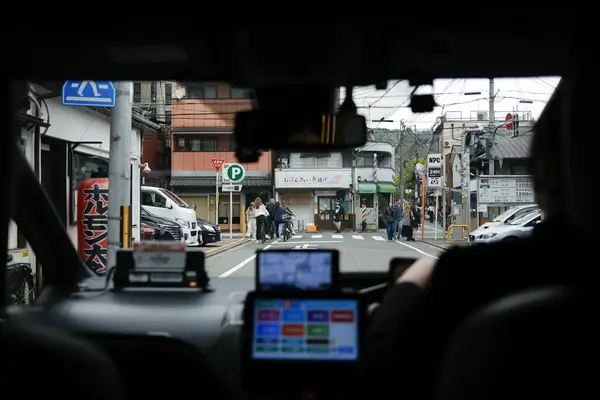 A view from a car on a street with buildings and pedestrians in Kyoto Japan