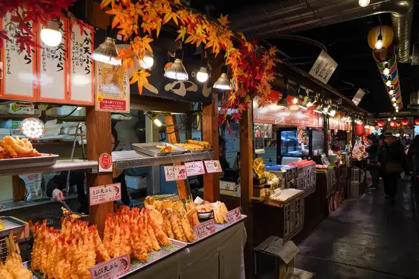 A food stall in Nishiki Market Kyoto offering tempura and other dishes under a decorative canopy of leaves