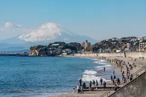 Seaside view with people walking along the beach and Mount Fuji visible in the background