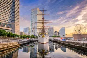 Tall ship docked in an urban waterfront area modern buildings and a Ferris wheel in the background
