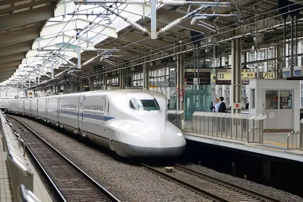 A highspeed train at a station platform viewed from track level with passengers and infrastructure visible