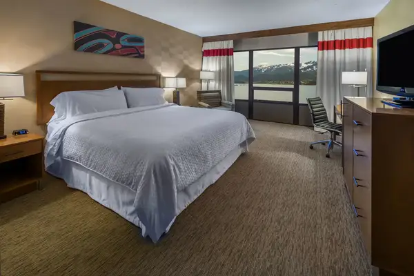 A hotel room with a large bed, nightstands, and a view of mountains through glass doors