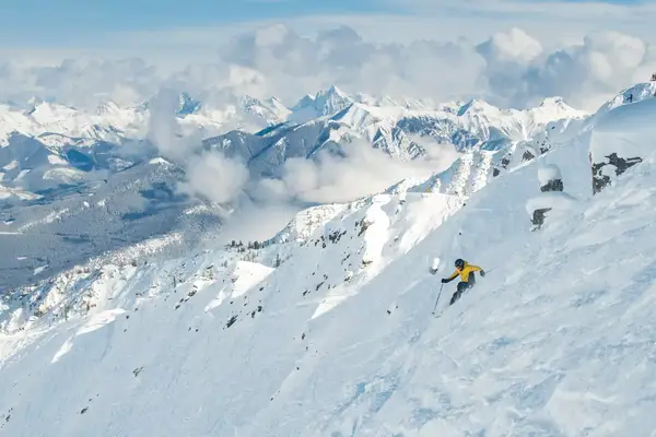 Person skiing down snow-covered mountain with mountains in the background. 
