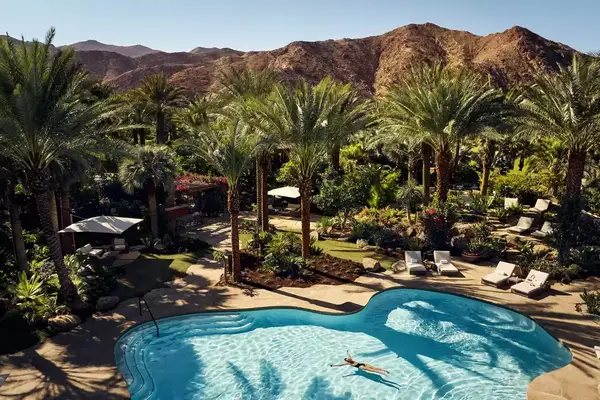 Aerial view of large swimming pool surrounded by palm trees with mountains in the distance at Sensei Porcupine Creek in California
