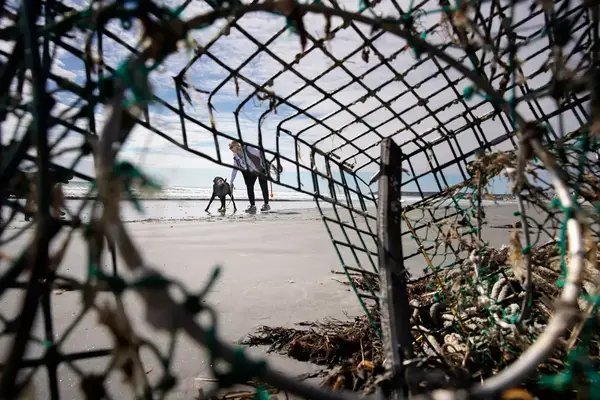 Seen through a lobster trap that washed ashore, a woman and a dog walk on Long Sands Beach in York