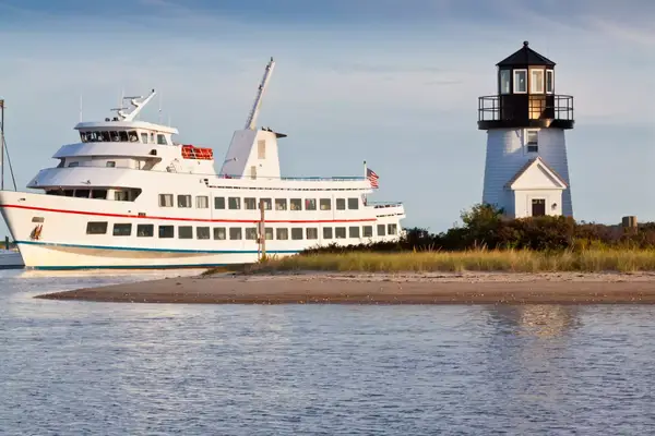 A ferry boat sailing near a coastline with a lighthouse in view, surrounded by shrubs and the ocean