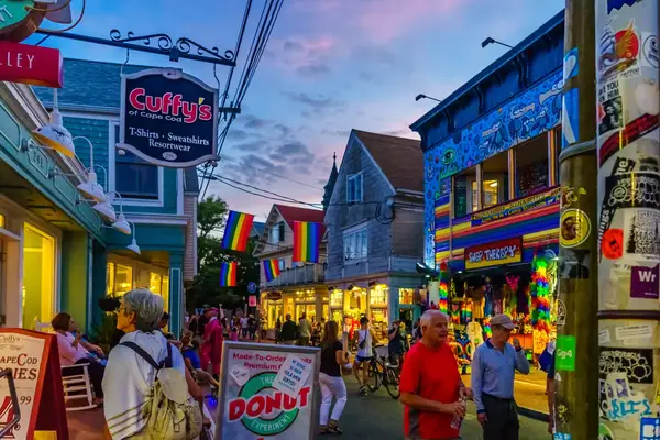A lively street scene with shops and people walking, featuring colorful banners and signs in a Cape Cod area