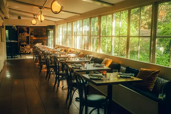 Empty restaurant interior with set dining tables and large windows overlooking greenery