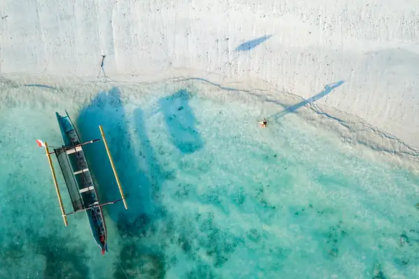 Aerial view of a person near a canoe in shallow clear water on a sandy shoreline