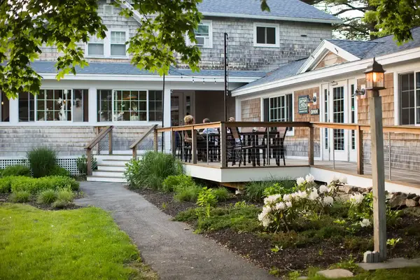 Outdoor seating area at a restaurant with a wooden deck and nearby garden, part of a building with large windows