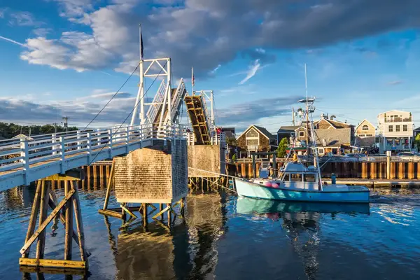 A wooden drawbridge over water with buildings in the background, a boat near the bridge in a harbor setting