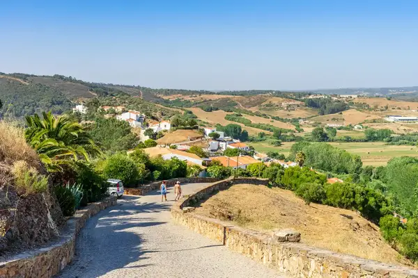 Rural landscape with a cobblestone path leading downhill surrounded by greenery buildings and people walking in the distance