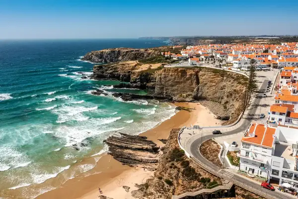 A coastal town with houses atop cliffs overlooking a beach and ocean waves