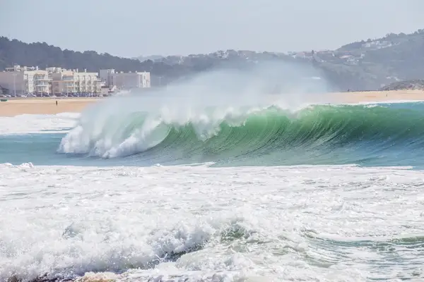 Ocean waves crashing near a coastal town with hills in the background