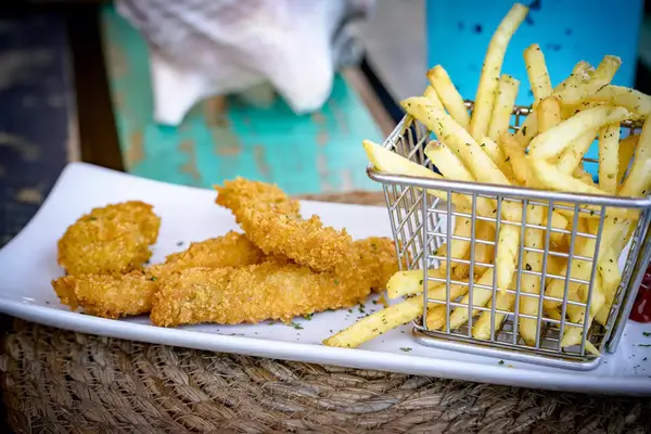 Crispy breaded fish sticks served with seasoned fries in a wire basket on a white plate