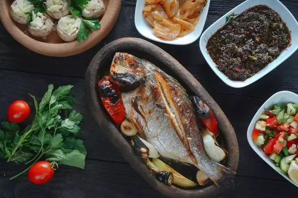 A roasted fish served with garnish and accompanying side dishes on a dark table