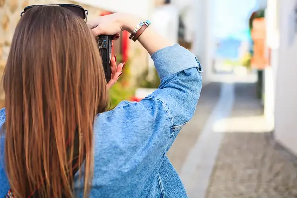 A person holding a camera and facing a narrow outdoor pathway