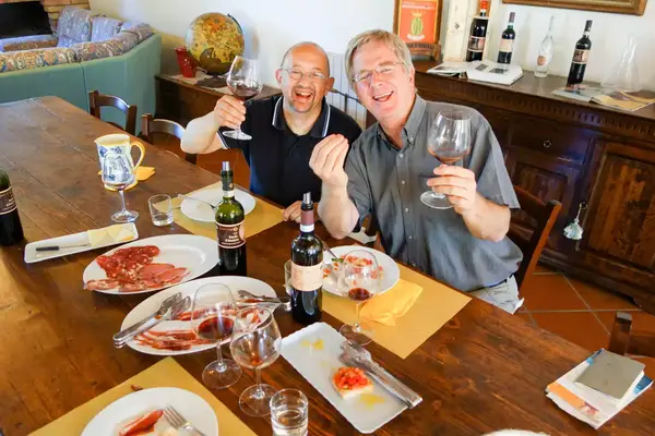 Rick Steves with wine and meat and a friend at a dining table