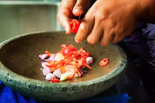 Indonesian Ayam Goreng preparation slicing chilies in mortar, mixing them with shallots and garlic