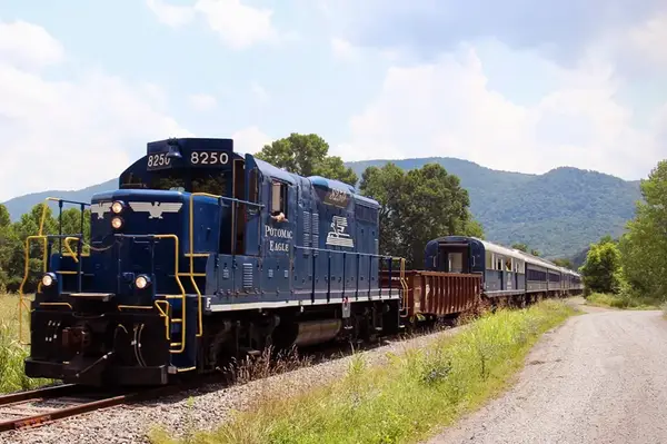 A blue locomotive pulling a train on a scenic rural railway with hillside in the background