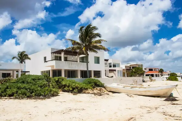 Mexican beach houses with boat and sea grass under bright blue sky with clouds