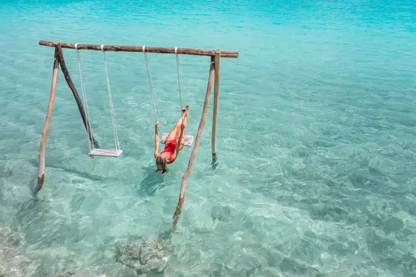 View of woman swinging on white sand beach relaxing and sunbathing by the lagoon in Mexico
