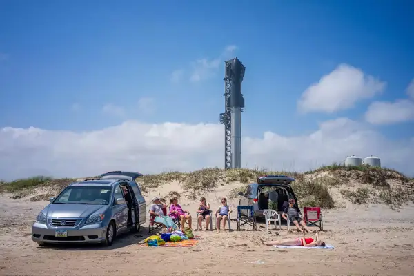 People spend time on the beach near the Starship Flight 3 Rocket a day before its scheduled launch at the Starbase facility near Boca Chica beach 