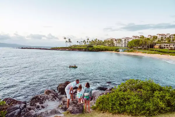 A family standing on a rocky coastline watching a sunset in Maui