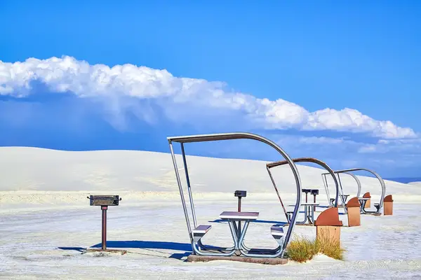 Picnic tables with shade structures and grills in a sandy desert landscape