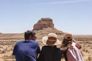 Three people facing a large rock formation in a desert
