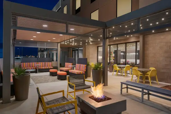 A patio seating area with a fire pit arranged under a pergola with string lights visible at a Hilton hotel