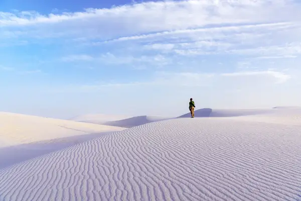 A lone person walking on sand dunes under a bright blue sky