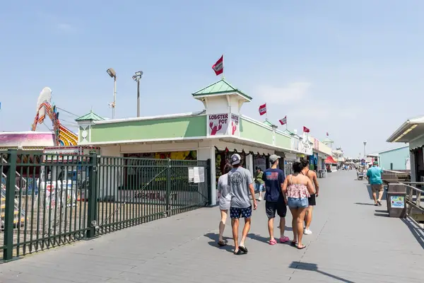 A group of people walking on a boardwalk near shops and attractions