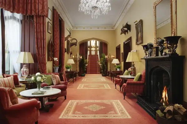 Elegant interior of a hall with a fireplace chandeliers and red furnishings leading to a staircase