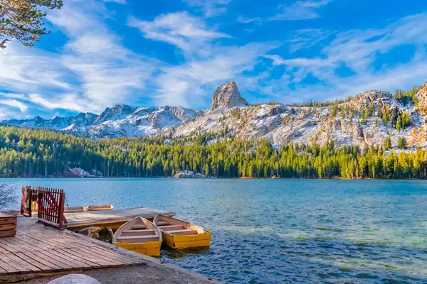 landscape of a small dock by a lake with snowy mountains in the background on a sunny day