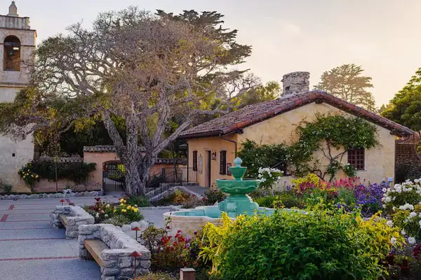 view of fountain surrounded by small garden and a small house in the background