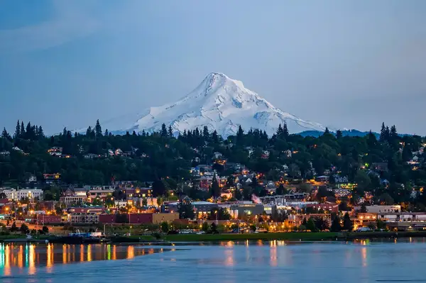 View of a town with a prominent mountain in the background, situated by a body of water, likely in the Columbia River Gorge region