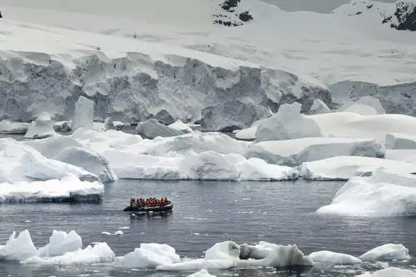 A group of people in red jackets on board a zodiac cruising in iceberg filled waters
