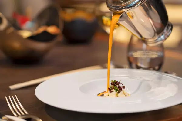 Pumpkin soup being poured over scallops and bacon in the restaurant of a luxury hotel