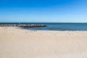 View of a sandy beach with calm ocean waves and a rock jetty in the distance