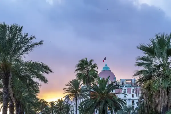 The dome of Le Negresco in Nice France surrounded by palm trees and set against a sunset sky