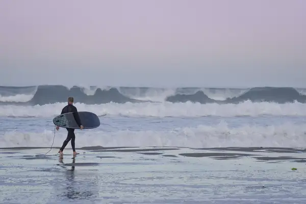 A surfer walking down Pacific Beach